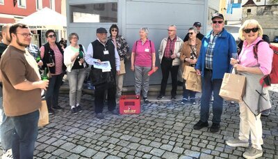 „Bier-Hopping durch Sulzbach-Rosenberg: Mehr als nur ein Schluck Geschichte!“ Sulzbach-Rosenberg, 23. April – Die Sonne schien, und die ersten Bierfreunde versammelten sich am Luitpoldplatz, um an der beliebten Führung von KulturAS teilzunehmen. Wer dachte, hier dreht sich alles nur um Bier, wurde schnell eines Besseren belehrt: Neben jeder Menge frisch gezapften Bieren gab es auch eine Vielzahl an Anekdoten und Geschichten, die für so manches Schmunzeln sorgten. Veranstalter Walter Heldrich hieß die Gruppe am historischen Löwenbrunnen willkommen. Gemeinsam mit den Gästeführern Monika und Peter Preller begab sich die Truppe auf eine kurzweilige Zeitreise durch die jahrhundertealte Braukultur der Stadt. Zum Auftakt erhielt jeder ein funkelndes Bierglas – und direkt am Platz wurde das erste „Fuchsbeck“-Bier verkostet. Anschließend erzählten die Prellers von der Blütezeit der Sulzbacher Brauereien. Erste Station war der Sperber Bräu: Dort erklärte der diplomierte Biersommelier Michael Sperber bei einer Zoigl Verkostung, wie die Spezialitäten der Brauerei nach dem „Reinheitsgebot“ gebraut werden und wie die Brauerei für die Zukunft aufgestellt wird. Auf dem weiteren Weg durch die Altstadt führte die Tour an den einstigen Bierlieferanten Schinhammer, an der Bäckerei & Bierschenke Kreiner, am Tucherdepotstüberl und am Ratskeller vorbei. Peter Preller ließ die Geschichten der verschwundenen Schänken lebendig werden und machte deutlich, wie eng die Orte einst mit dem gesellschaftlichen Leben verwoben waren. Im „Bayerischen Hof“, einer ehemaligen Brauerei, gewährte Gastgeber Georg Eberwein Einblicke in fast 200 Jahre Familiengeschichte. Er spannte den Bogen von den Gründergenerationen Renner und Seitz bis zur heutigen Familie Eberwein und zeigte, wie Familientradition und handwerkliches Können die Braukunst über Jahrzehnte prägten. Anschließend führte der Weg die Gruppe weiter zur Fuchsbeck-Brauerei, und nach nur wenigen Schritten bestaunte man das mächtige 12 Hektoliter Fass. Peter Preller erläuterte, wie die Familie Fuchs 1820 von der Bäckerei zum Brauhaus wechselte und das Braurecht später an die Familie Orth überging. Den krönenden Abschluss bildete das Gasthaus „Zur Landkutsche“ (Pamler-Wirtschaft) an der alten Nürnberger Straße, wo Christian Kellner von der Gründung um 1400, dem Brand im Landshuter Erbfolgekrieg 1504 und dem Wiederaufbau im späten 16. Jahrhundert berichtete. Heute lockt ein schattiger Biergarten unter Kastanien, während drinnen ein König-Ludwig-Bild für urige Stimmung sorgt. Drei Kanonenkugeln mit der Inschrift MCCCC A.D. und eine Johannes Nepomuk-Statue an der Tür erinnern an das mittelalterliche Erbe.  Organisator Walter Heldrich dankte abschließend allen Mitwirkenden – insbesondere Martina Heiß, da die Landkutsche normalerweise nur Freitags geöffnet ist, extra für den Ausklang öffnete. Der Erlös der Führung kommt einer regionalen Wohltätigkeitsorganisation zugute.  Mit kurzweiligen Anekdoten, informativen Einblicken und frisch gezapften Bieren bot die Führung zum Tag des Bieres einen rundum gelungenen Streifzug durch die Biergeschichte Sulzbach Rosenbergs. Prost! 